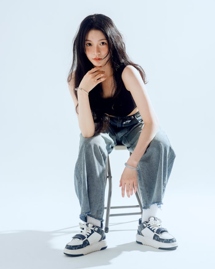 Young woman in casual attire poses confidently, seated on a chair in a modern setting.